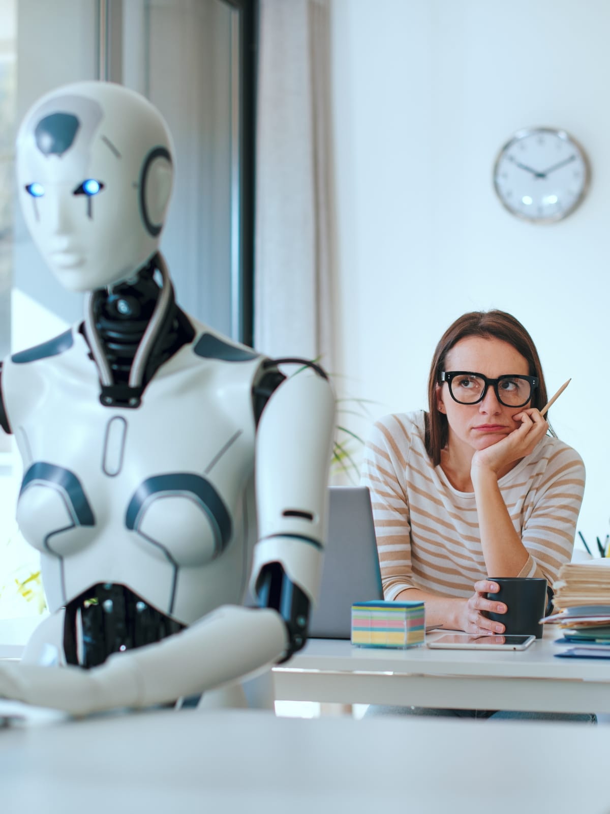 Office worker seated beside a robot, representing how AI-created capacity can affect workload and job design.